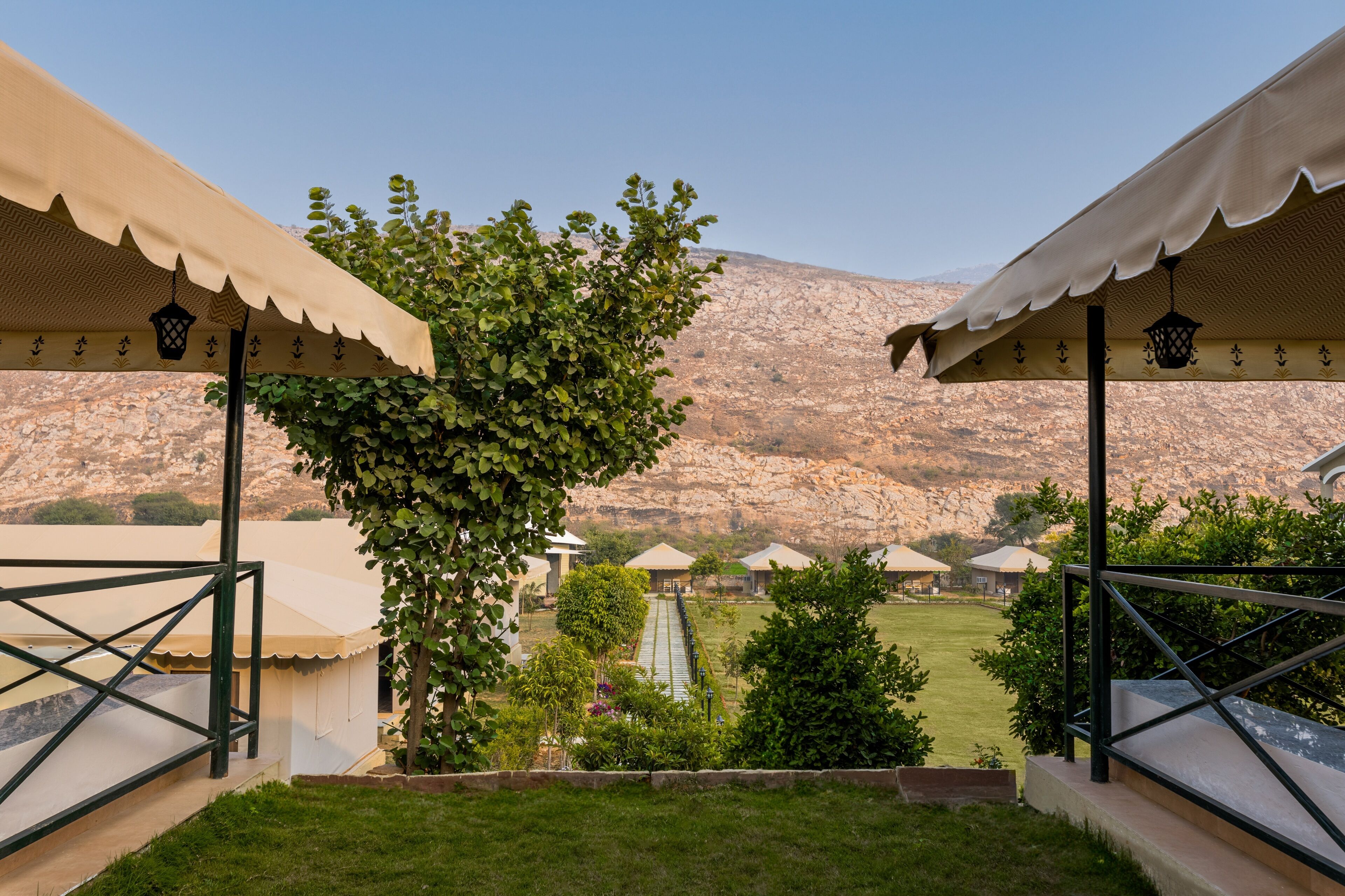 A view of a courtyard with a mountain backdrop, featuring a tree, a pathway, and several tents.