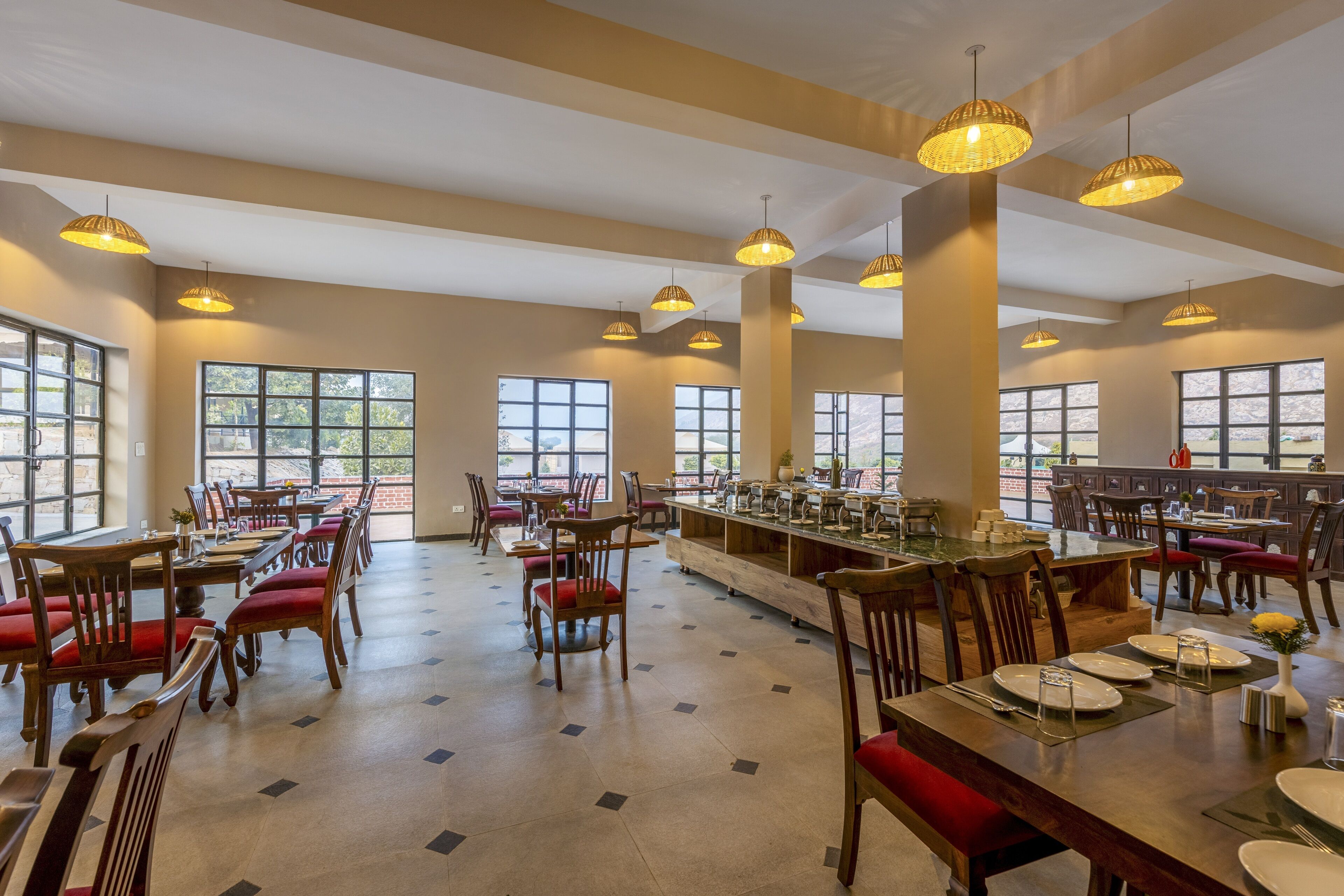 Un vaste espace dédié à la salle à manger, avec de nombreuses tables et chaises, de grandes fenêtres et des luminaires suspendus.