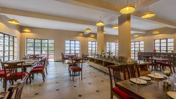 Un vaste espace dédié à la salle à manger, avec de nombreuses tables et chaises, de grandes fenêtres et des luminaires suspendus.