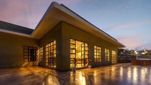 A modern building with large windows and a flat roof, featuring a well-lit entrance and a paved area in front. - Sterling ReWild Sariska (Thanagazi)
