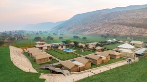 A resort with multiple bungalow-style buildings, a central swimming pool, and a hilly backdrop. - Sterling ReWild Sariska (Thanagazi)