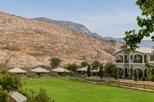Un hotel con un amplio césped, varias edificaciones con ventanas arqueadas y un paisaje montañoso al fondo.