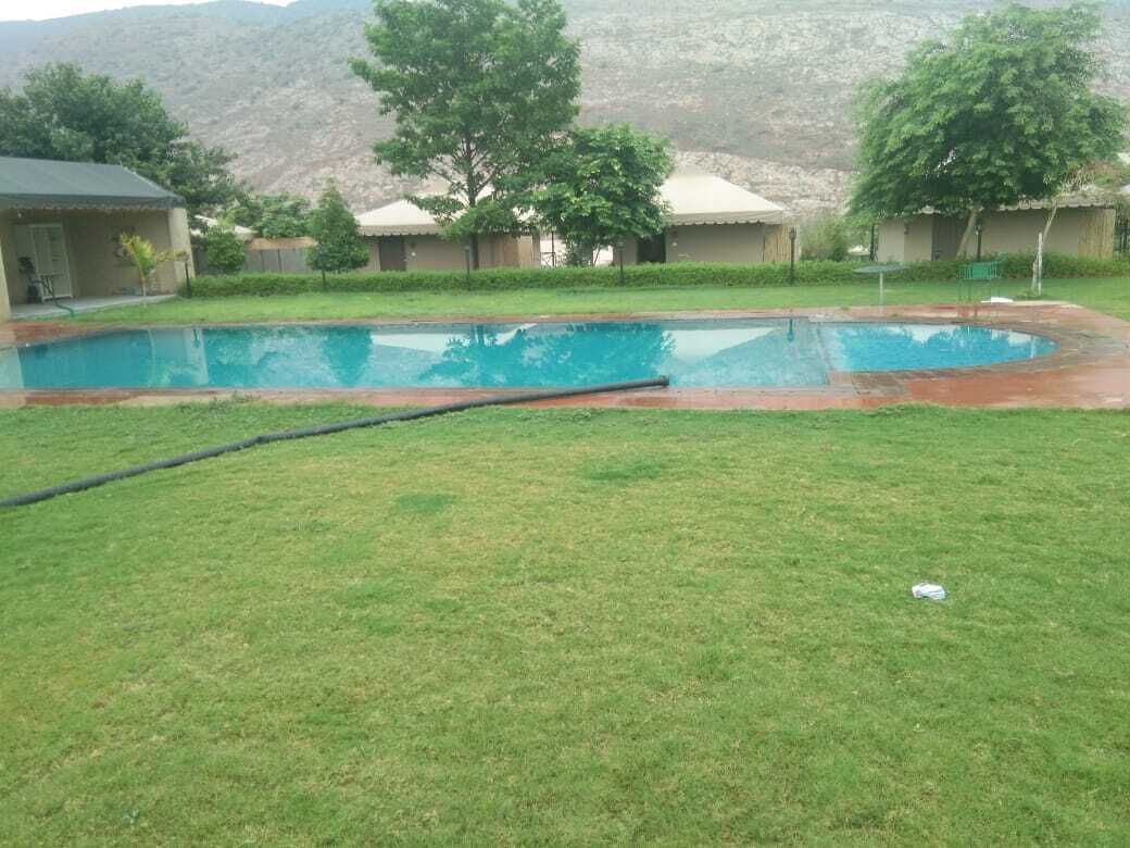 A swimming pool with a grassy area in front, surrounded by buildings with a mountainous backdrop.