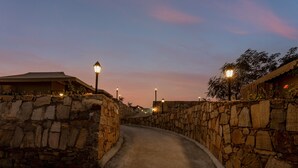 A stone-walled pathway leading to a building with a roof. Street lamps line the path. - Sterling ReWild Sariska (Thanagazi)