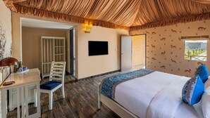 A bedroom with a bed, a desk, and a chair. There is a television on the wall and a window with a view. - Sterling ReWild Sariska (Thanagazi)