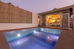 A swimming pool with a tiled floor, a bamboo fence, and a room with a bed and chairs visible through a glass door.