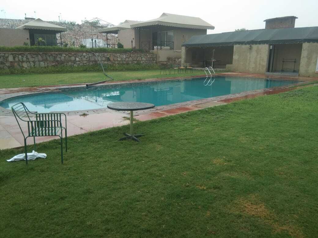 Une piscine avec un fauteuil de relaxation et une petite table, entourée d’une pelouse verdoyante et d’un mur de pierres.