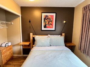 Une chambre à coucher avec un lit, une commode en bois, un porte-manteau mural et un tableau encadré accroché au mur.
