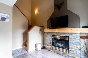 Un interior moderno con chimenea, una escalera de madera y un televisor montado.