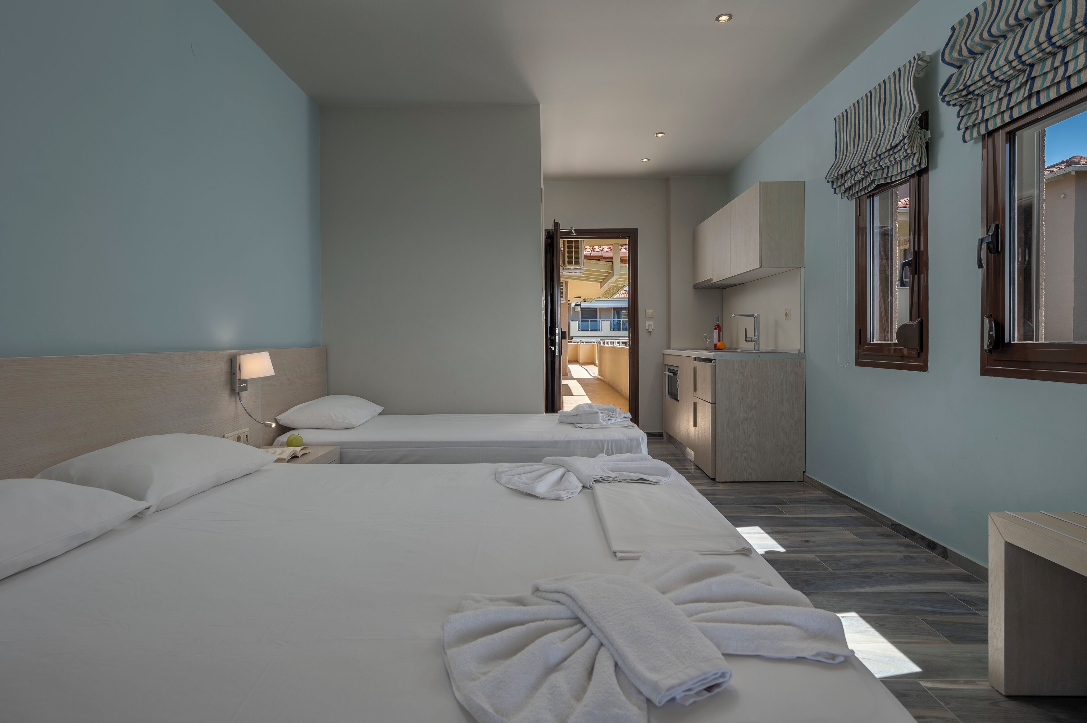 A hotel room with two beds, a small kitchenette, and a view of the outside.