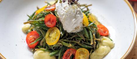 A plate of food with green beans, cherry tomatoes, and a dollop of cream on top.