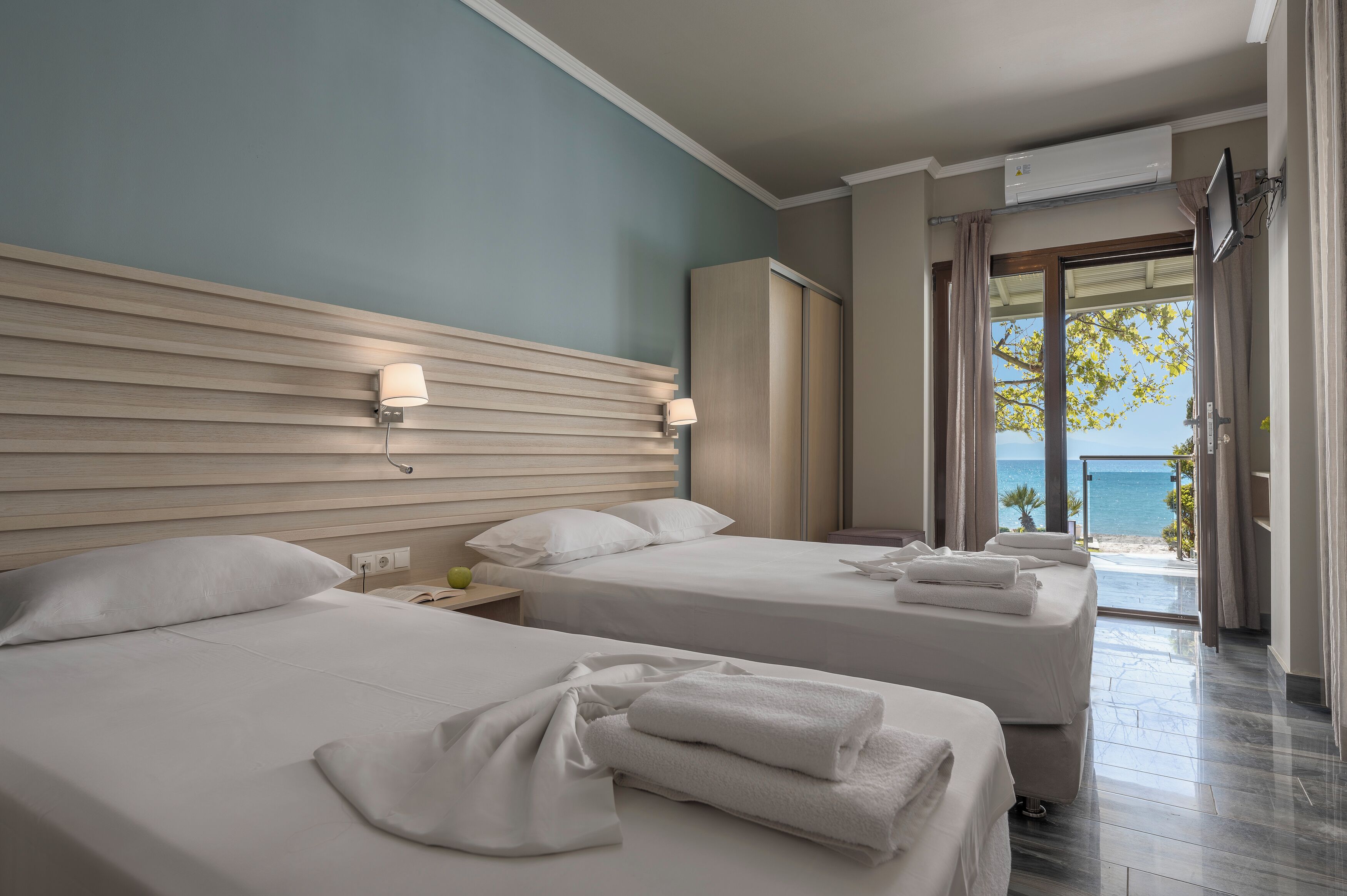 Une chambre d’hôtel avec deux lits, une vue sur la mer, un ventilateur de plafond et un téléviseur fixé au mur.