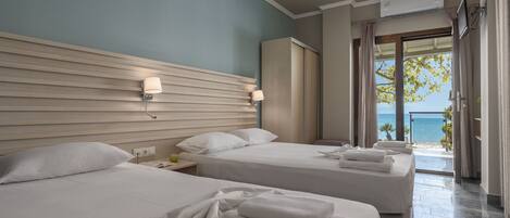 A hotel room with two beds, a view of the sea, a ceiling fan, and a TV mounted on the wall.