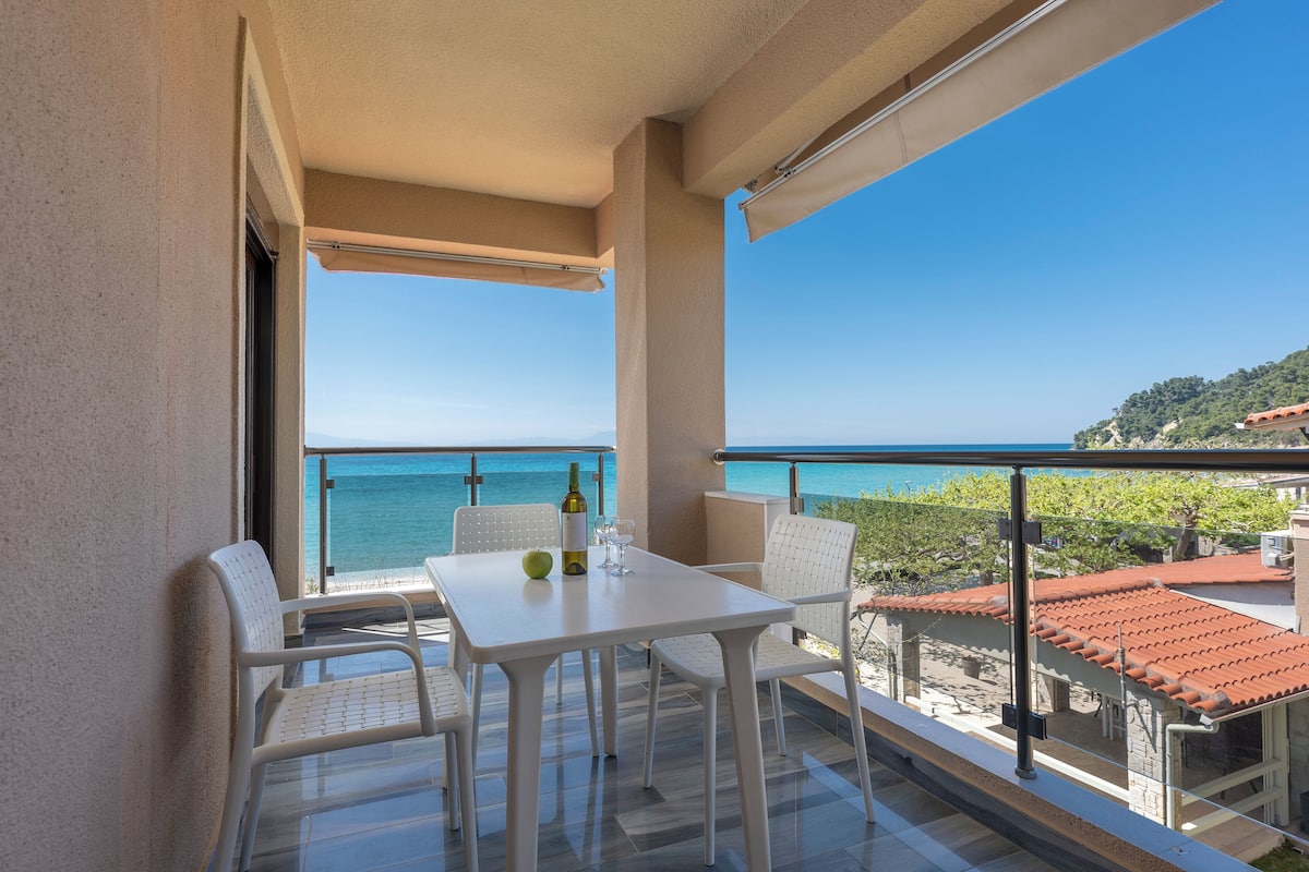 Ein Balkon mit Tisch und Stühlen mit Blick auf einen Strand und das Meer.