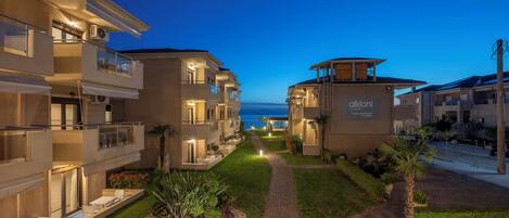 A modern hotel with multiple balconies, a well-maintained garden, and a view of the sea.