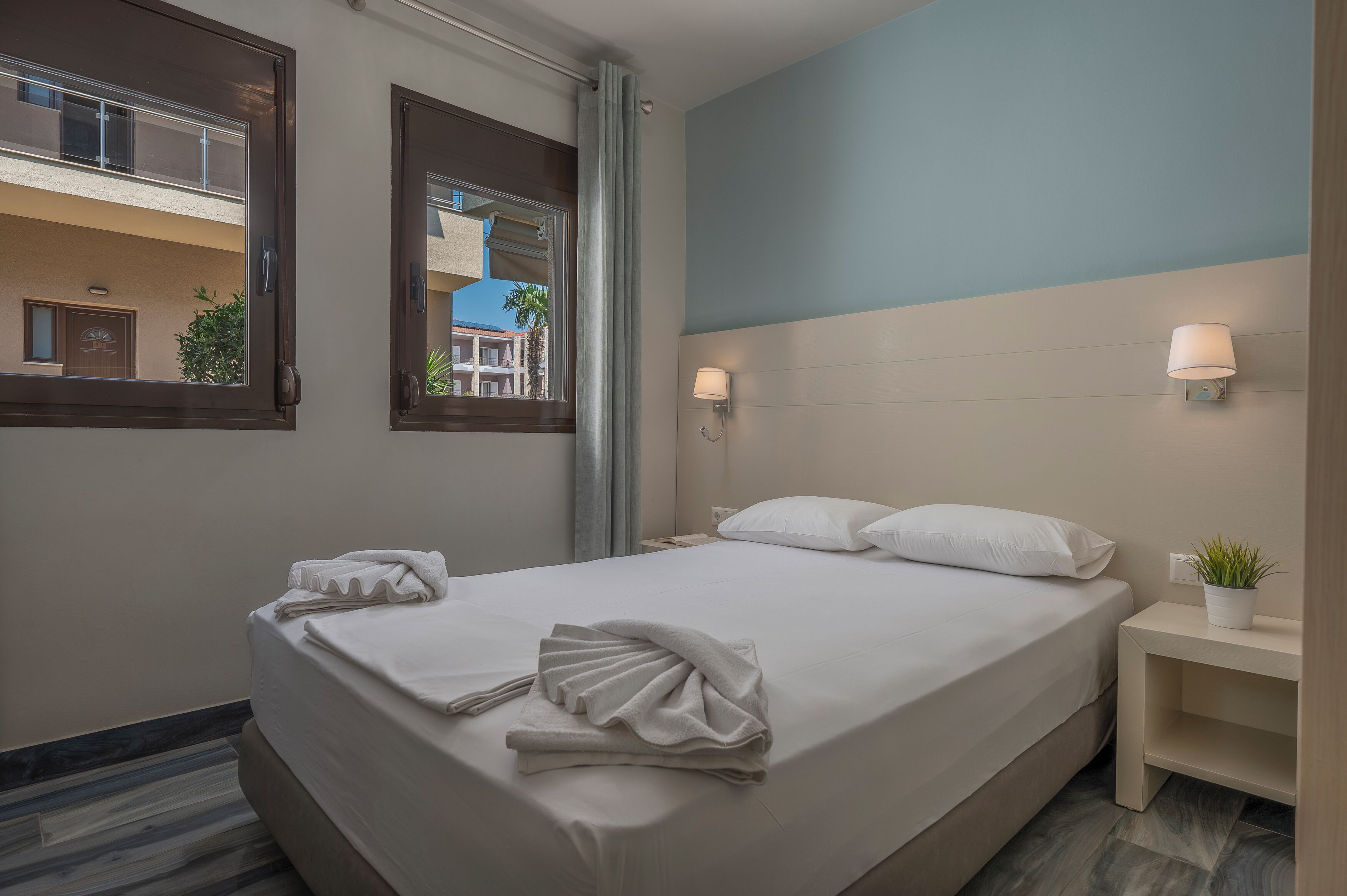 Une chambre d’hôtel avec un lit, une table de chevet, une lampe fixée au mur et une fenêtre avec des rideaux.