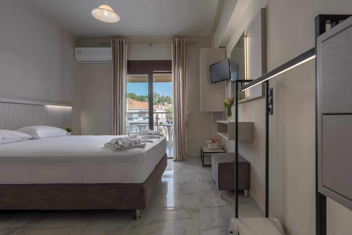 Ein modernes Hotelzimmer mit einem großen Bett, einem Fernseher, einem kleinen Tisch mit einer Lampe und Blick ins Freie.