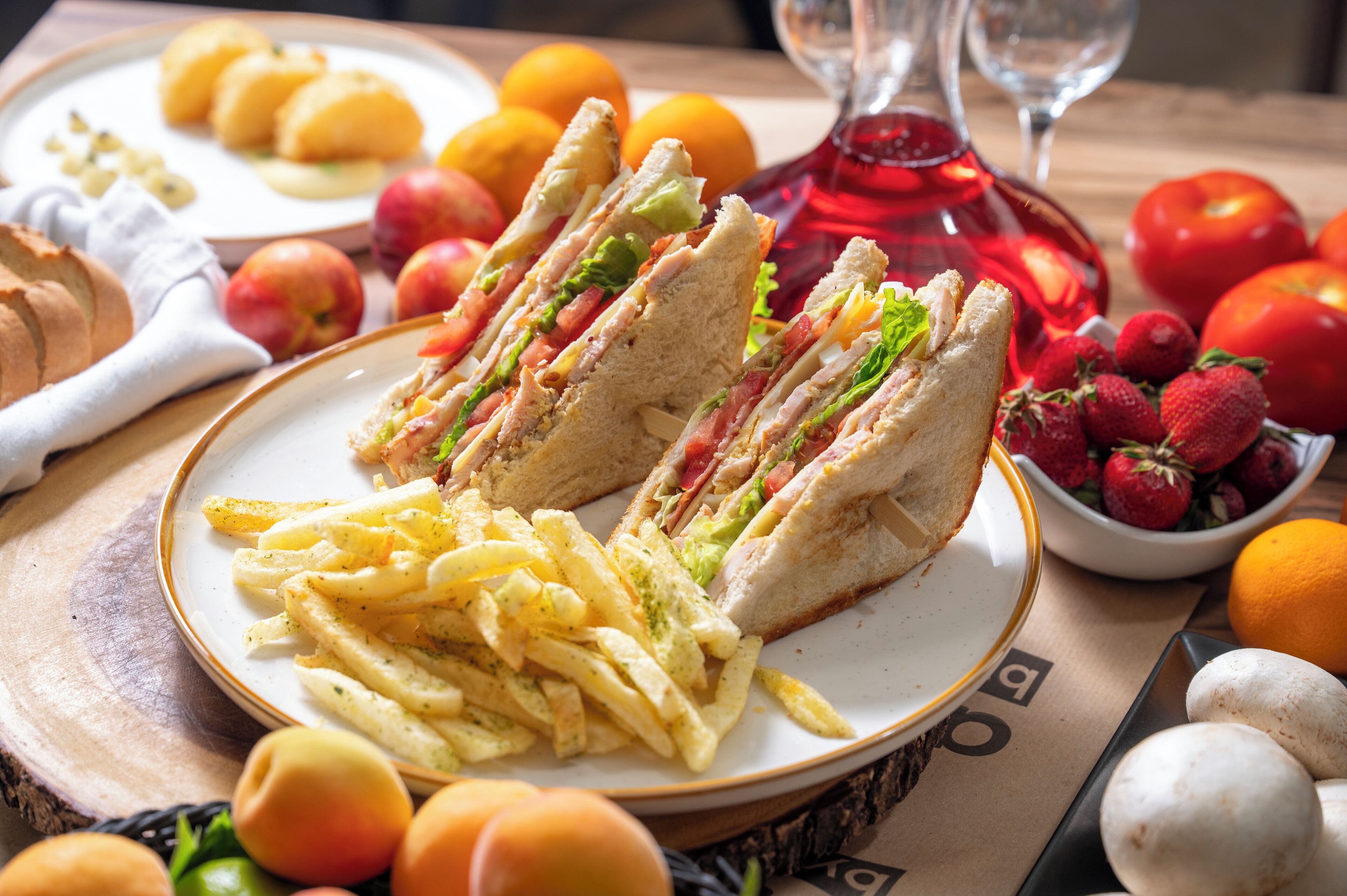 Ein Teller mit Sandwiches, Pommes und Obst auf einem Tisch.