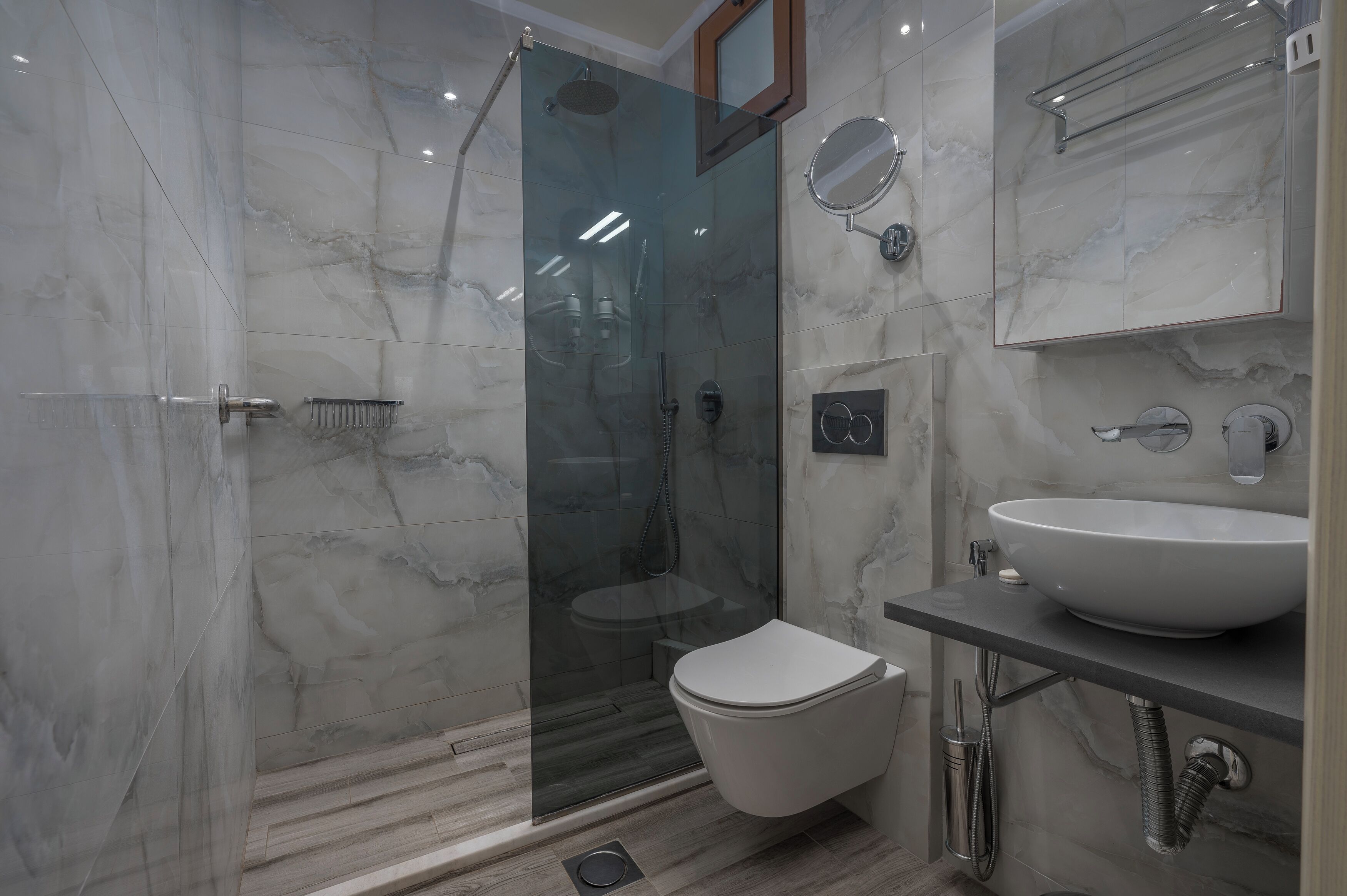 Ein modernes Badezimmer mit einer in Glas eingefassten Dusche, einer weißen Toilette und einem мраморном Waschbecken.