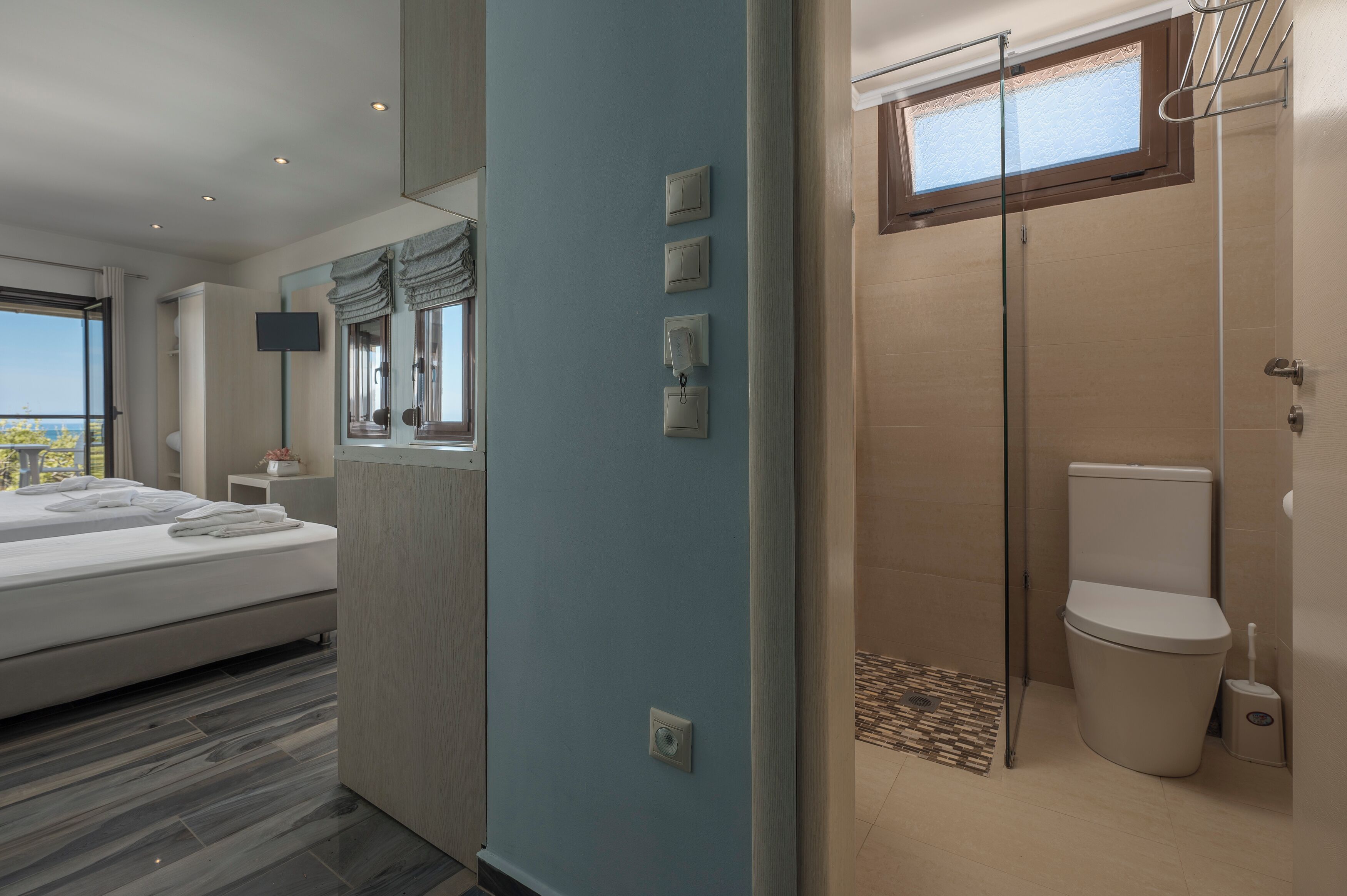 A modern hotel room with a bed, a bathroom with a toilet and shower, and a large window offering a view.