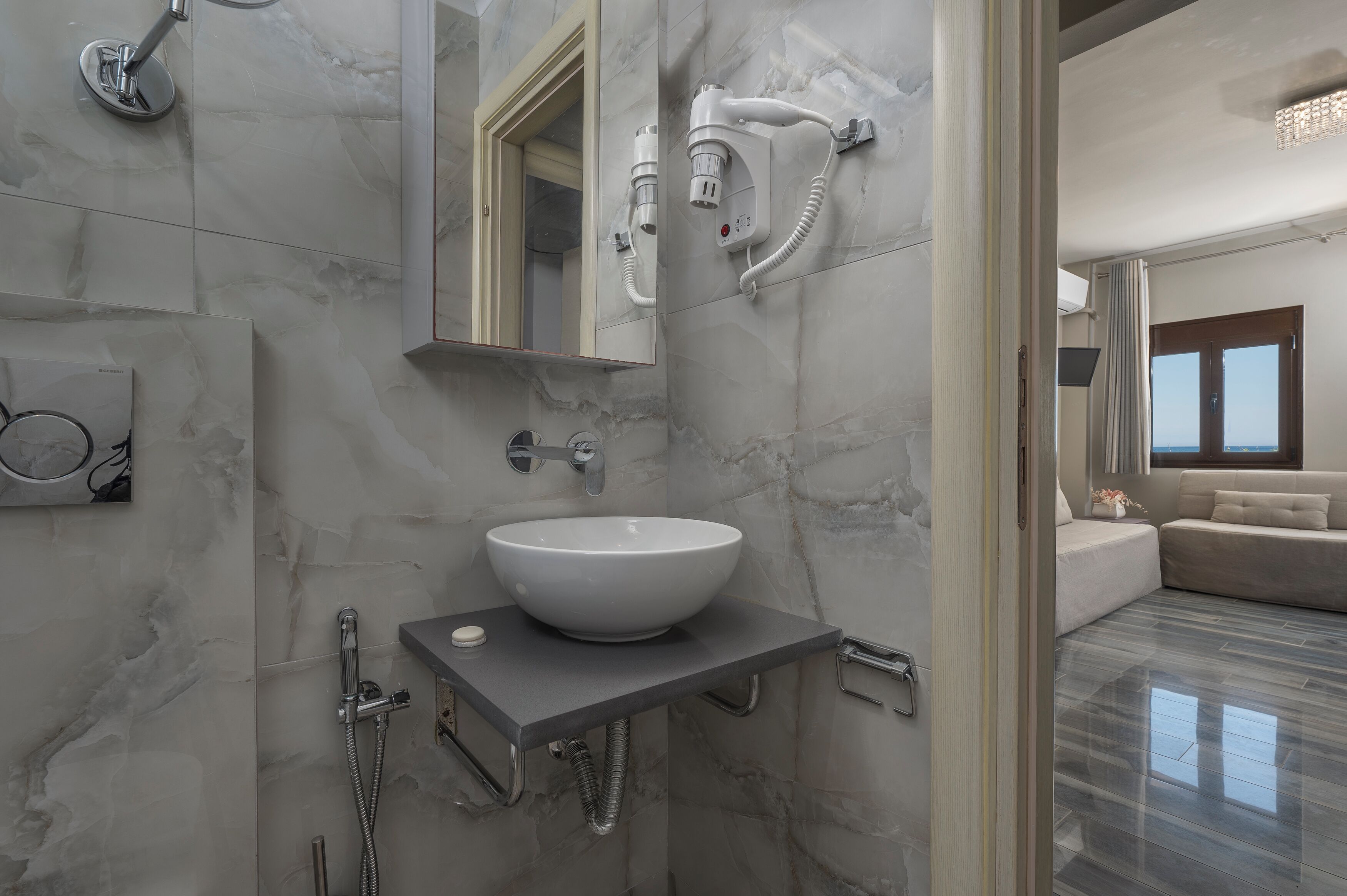 A modern bathroom with a marble sink, a handheld showerhead, and a hairdryer mounted on the wall.