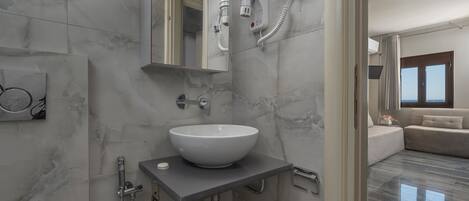A modern bathroom with a marble sink, a handheld showerhead, and a hairdryer mounted on the wall.