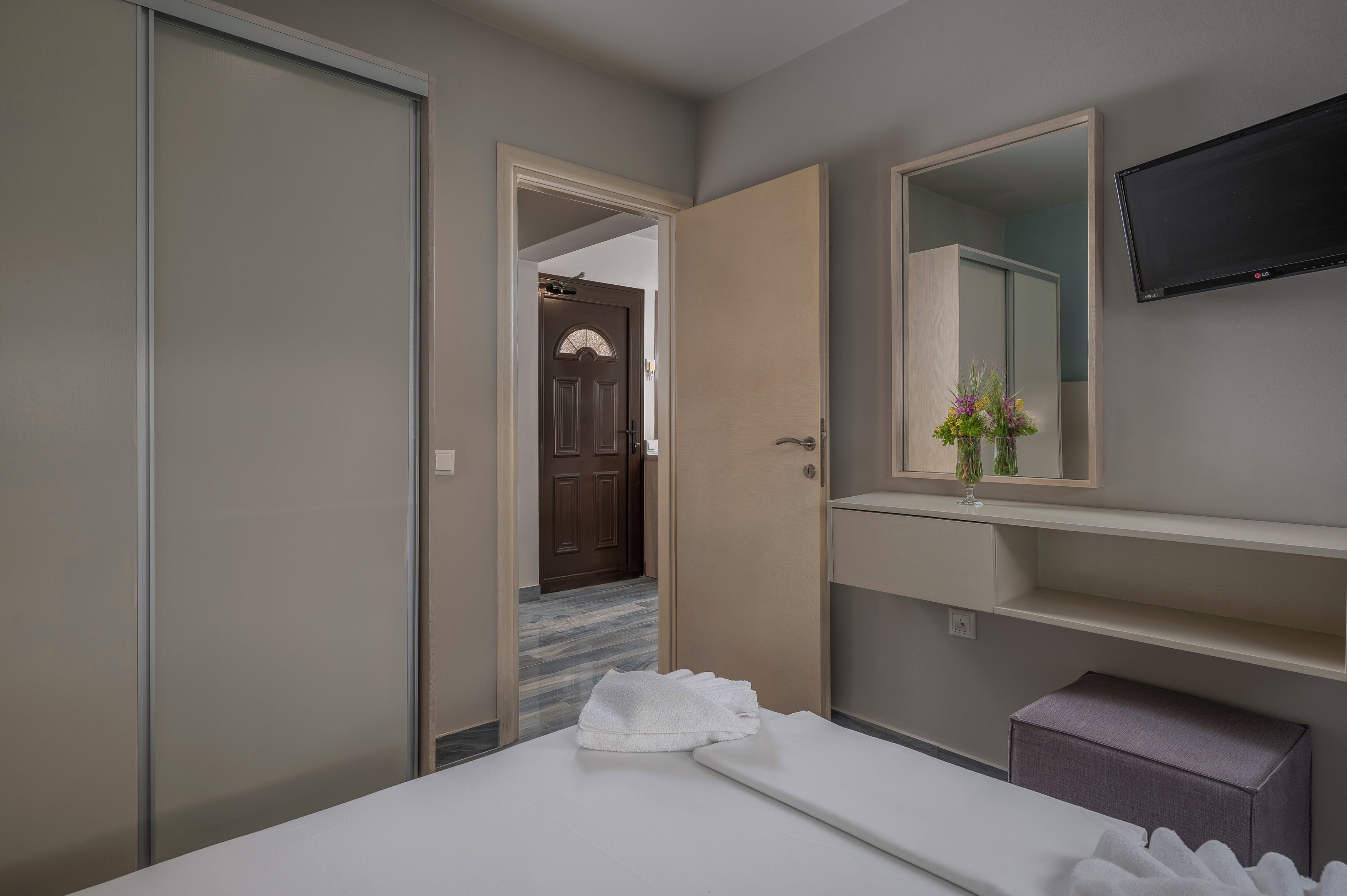 Une chambre d’hôtel avec un lit, un grand miroir, un téléviseur à écran plat et une petite table sur laquelle est posé un vase de fleurs.