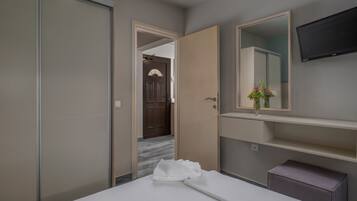 Une chambre d’hôtel avec un lit, un grand miroir, un téléviseur à écran plat et une petite table sur laquelle est posé un vase de fleurs.