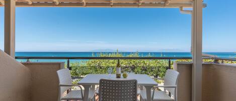 A covered outdoor seating area with a table and chairs, overlooking a scenic view of the sea and mountains.