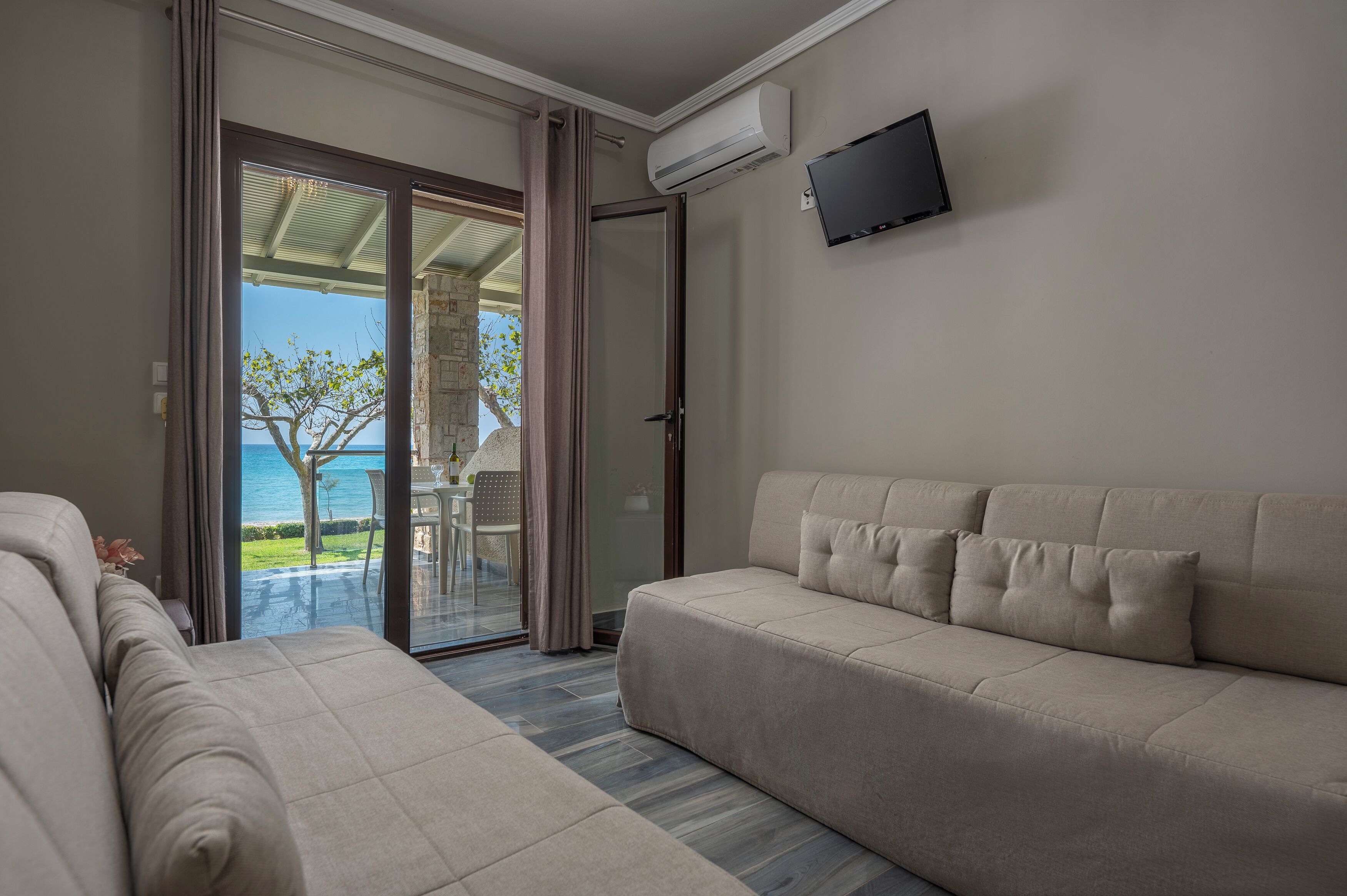 A modern living room with a sofa and a glass door leading to a balcony with a view of the sea.