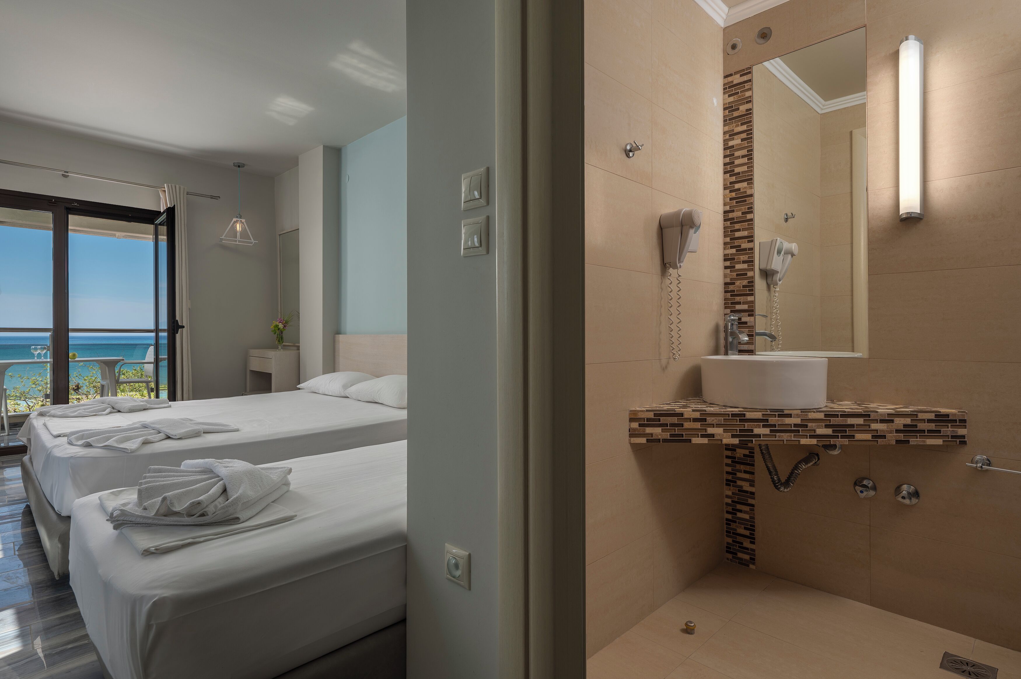 A hotel room with two beds, a bathroom with a shower, and a view of the sea.