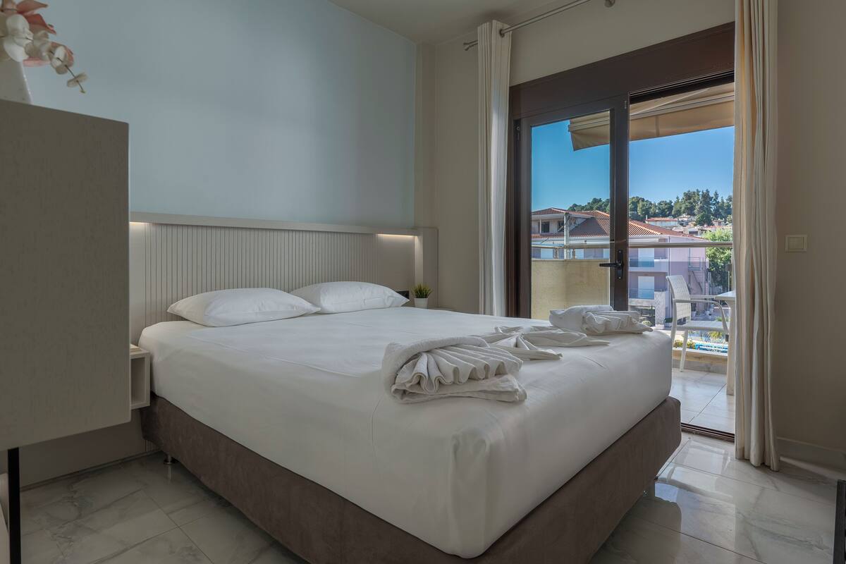 Ein modernes Hotelzimmer mit einem großen Bett, einem Nachttisch und Blick auf die Stadt durch eine Schiebetür.