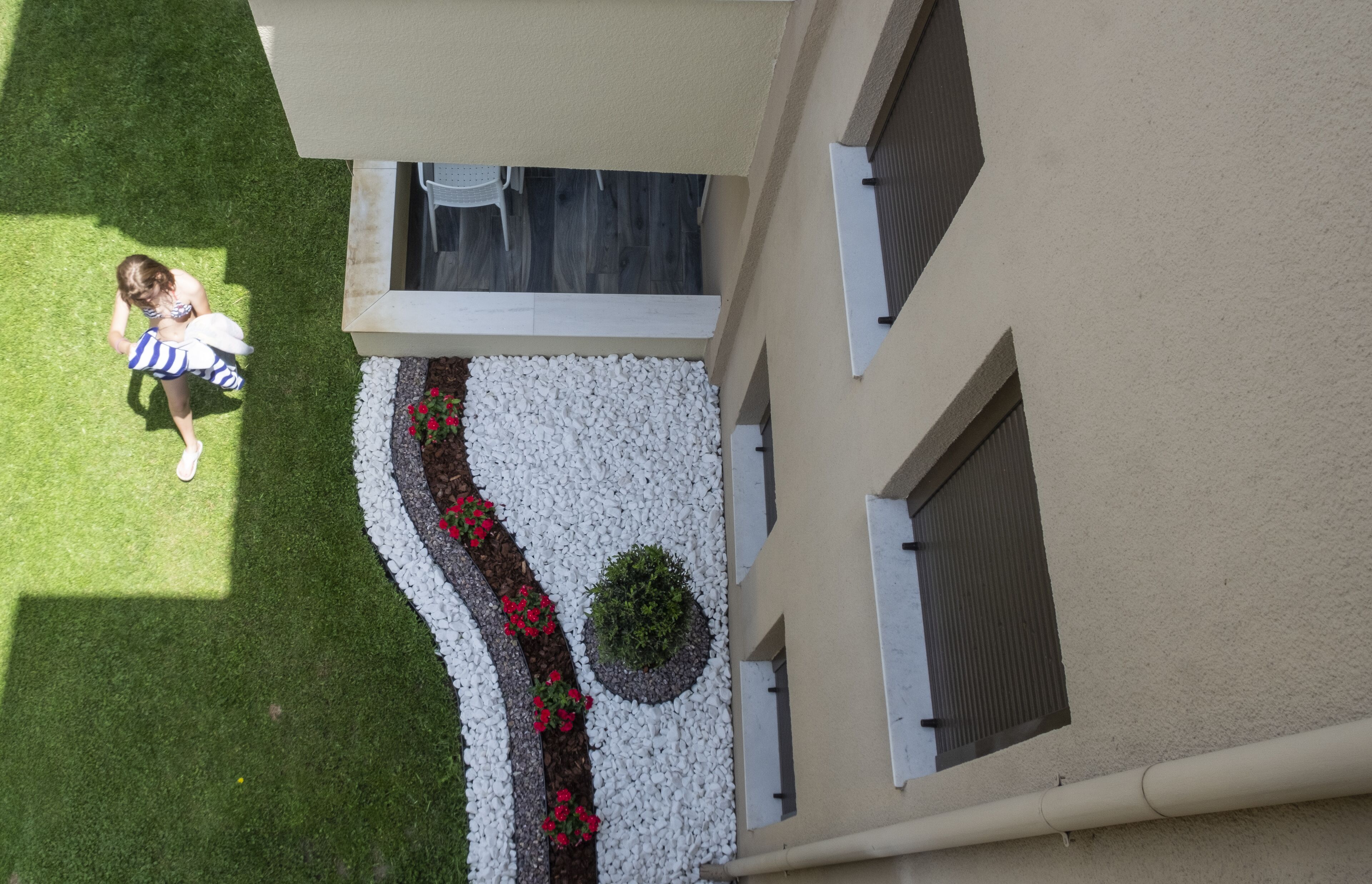 An aerial view of a building with a landscaped garden area featuring white pebbles, red flowers, and a small green bush.