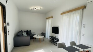 A modern living room with a sofa, TV, dining table, and chairs.