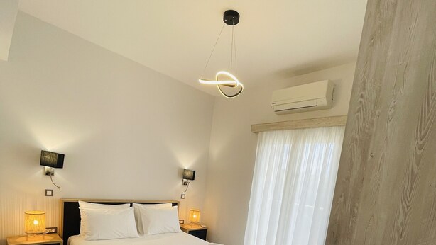 A hotel room with a bed, bedside lamps, a chair, and an air conditioning unit.