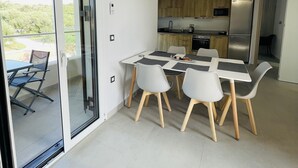 A modern kitchen with a dining area, featuring a sliding glass door to a balcony, a built-in oven, and a refrigerator.
