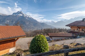 Una baita di legno con tetto in tegole rosse, un prato curato e vista sulle montagne innevate sullo sfondo.