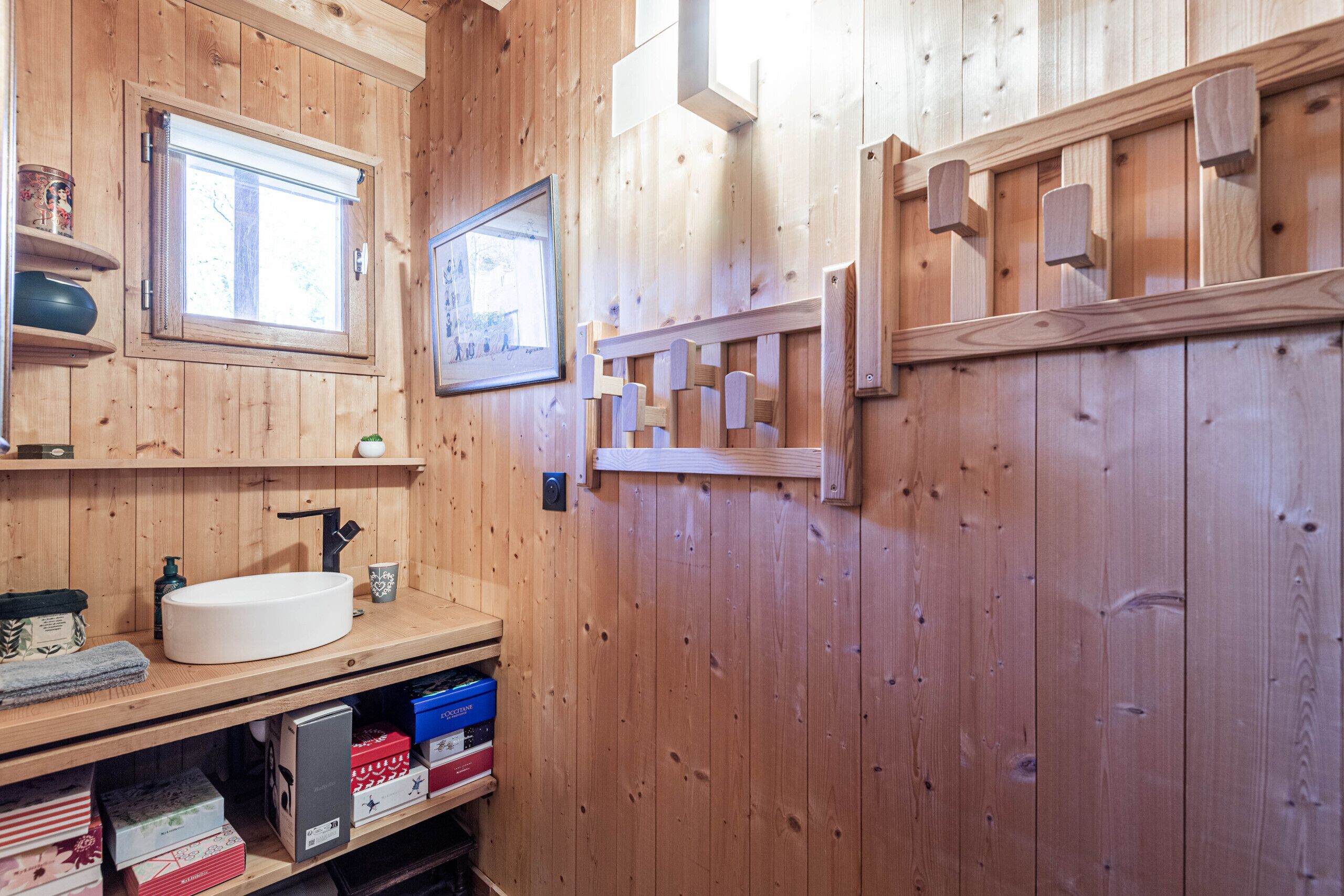 A wooden bathroom with a white sink, shelves with toiletries, and a framed picture on the wall.