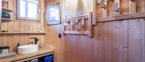 A wooden bathroom with a white sink, shelves with toiletries, and a framed picture on the wall.