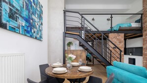 A dining area with a round table set for four, a staircase, and a teal sofa. - Stylish Studio with Mezzanine | Air Conditioning | Close to the Center (Kraków)