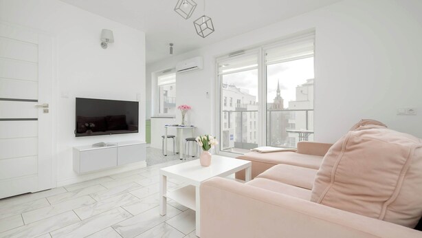 A modern living room with a flat-screen TV, a white coffee table, and a pink sofa.