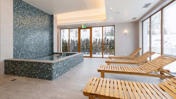 Un área de spa con pared de mosaicos, una bañera de hidromasaje y sillones de madera.