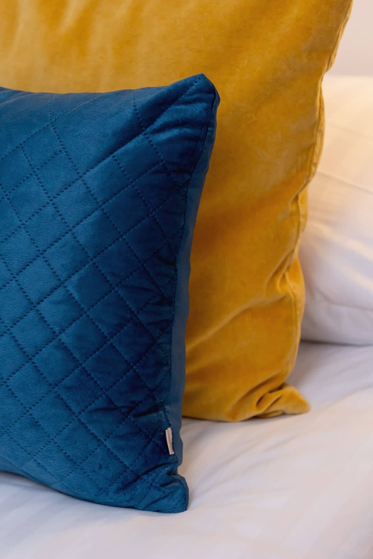 A bed with a blue quilted pillow and a yellow pillow.