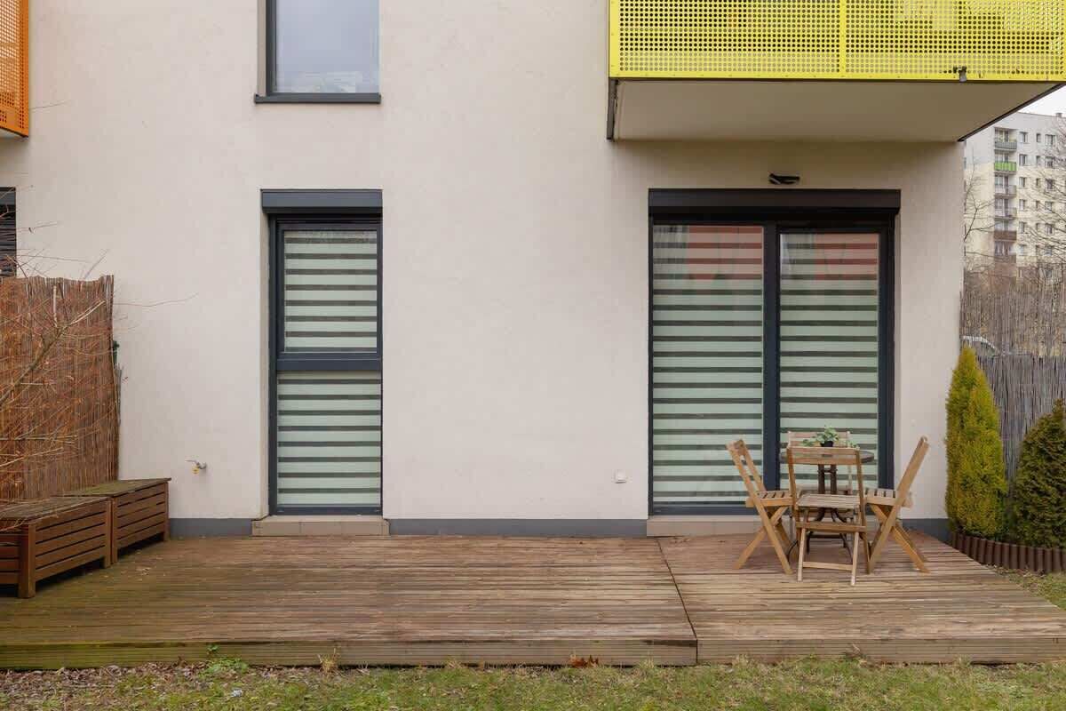 Un bâtiment moderne doté de deux grandes portes coulissantes, d’une terrasse en bois avec une table et des chaises, et d’un petit espace jardin.