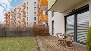 Un apartamento moderno con terraza de madera, mobiliario exterior y balcón con barandillas anaranjadas.