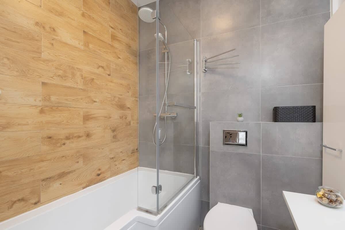 A modern bathroom with a wooden wall, a glass shower enclosure, a white bathtub, and a white toilet.