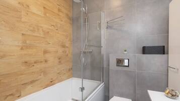 A modern bathroom with a wooden wall, a glass shower enclosure, a white bathtub, and a white toilet.