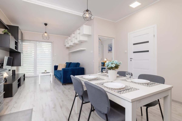 A closer look at the dining area, featuring a sleek white table, gray chairs, and decorative ceiling lighting, positioned next to the living room for an open feel.