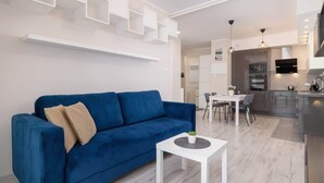 Una sala de estar moderna con un sofá azul, una mesa de centro blanca y una zona de comedor con mesa y sillas.
