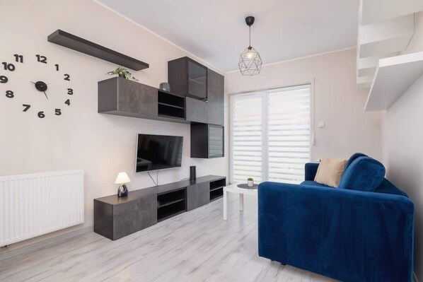 Una sala de estar moderna con un sofá azul, un televisor montado y una lámpara colgante de diseño geométrico.